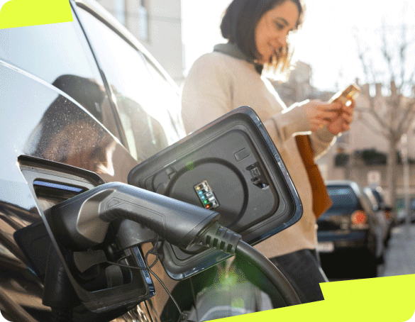 L'image montre une femme, accoudée sur sa voiture hybride ou électrique, en train d'attendre que son véhicule soit rechargé.