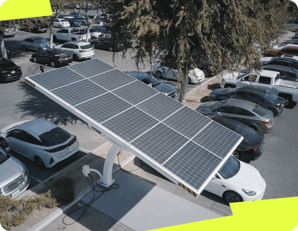 La photographie montre un parking vu en hauteur, qui accueille de nombreuses voitures et une ombrière photovoltaïque branché à une borne de recharge pour véhicule électrique.