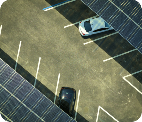 La photographie montre un parking vue de haut, ou deux véhicules sont stationnés en dessous d'ombrières photovoltaïques.